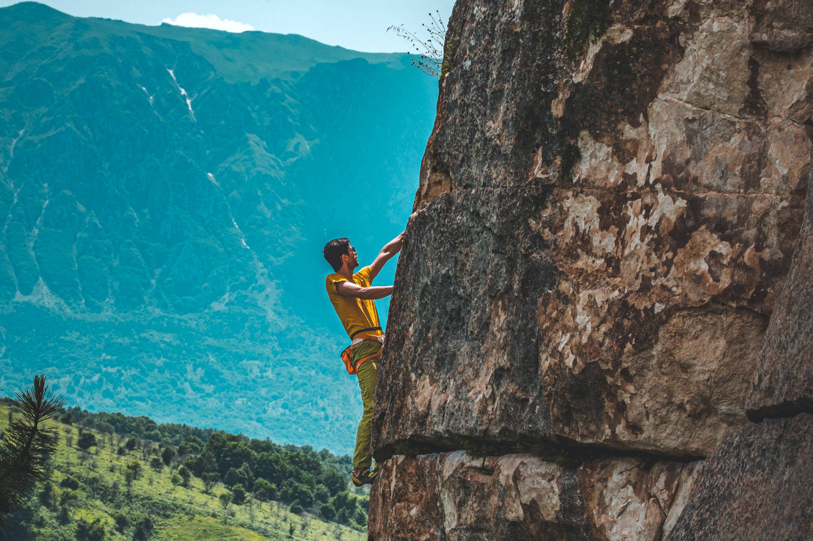 Alpinista in arrampicata su una parete rocciosa con vallata verde sullo sfondo